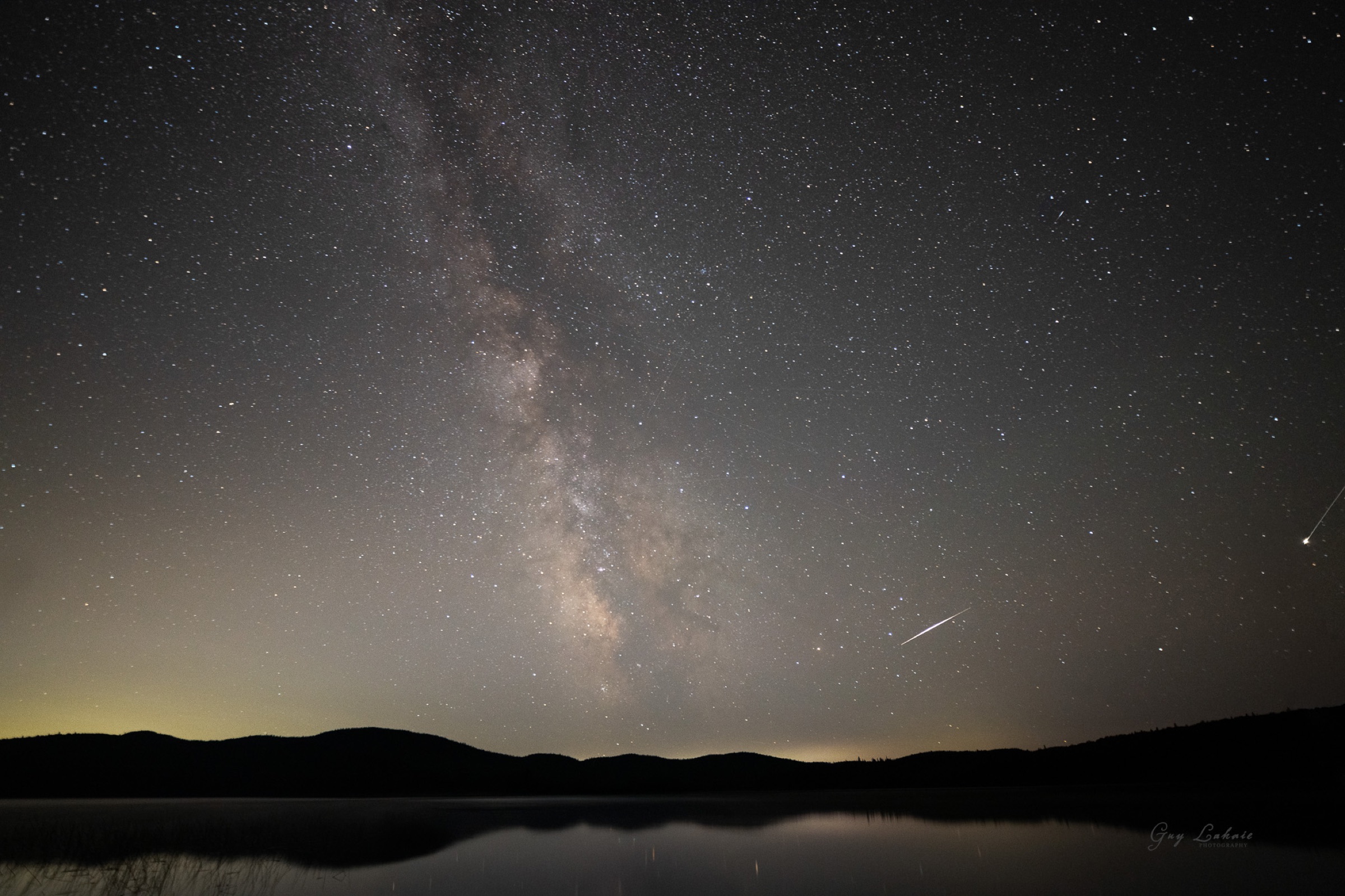 La Voie lactée se levant au-dessus d'un lac calme à Lac des Sables, Québec, avec une étoile filante traversant le ciel.