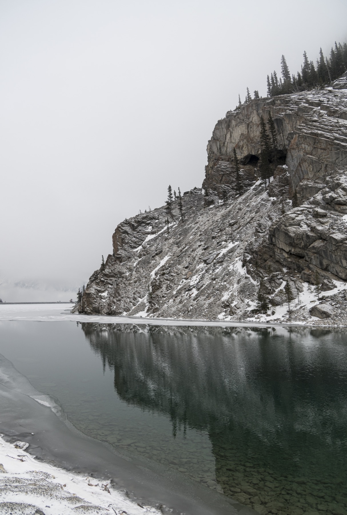 Falaise rocheuse enneigée se reflétant dans les eaux calmes d'un lac, Alberta.
